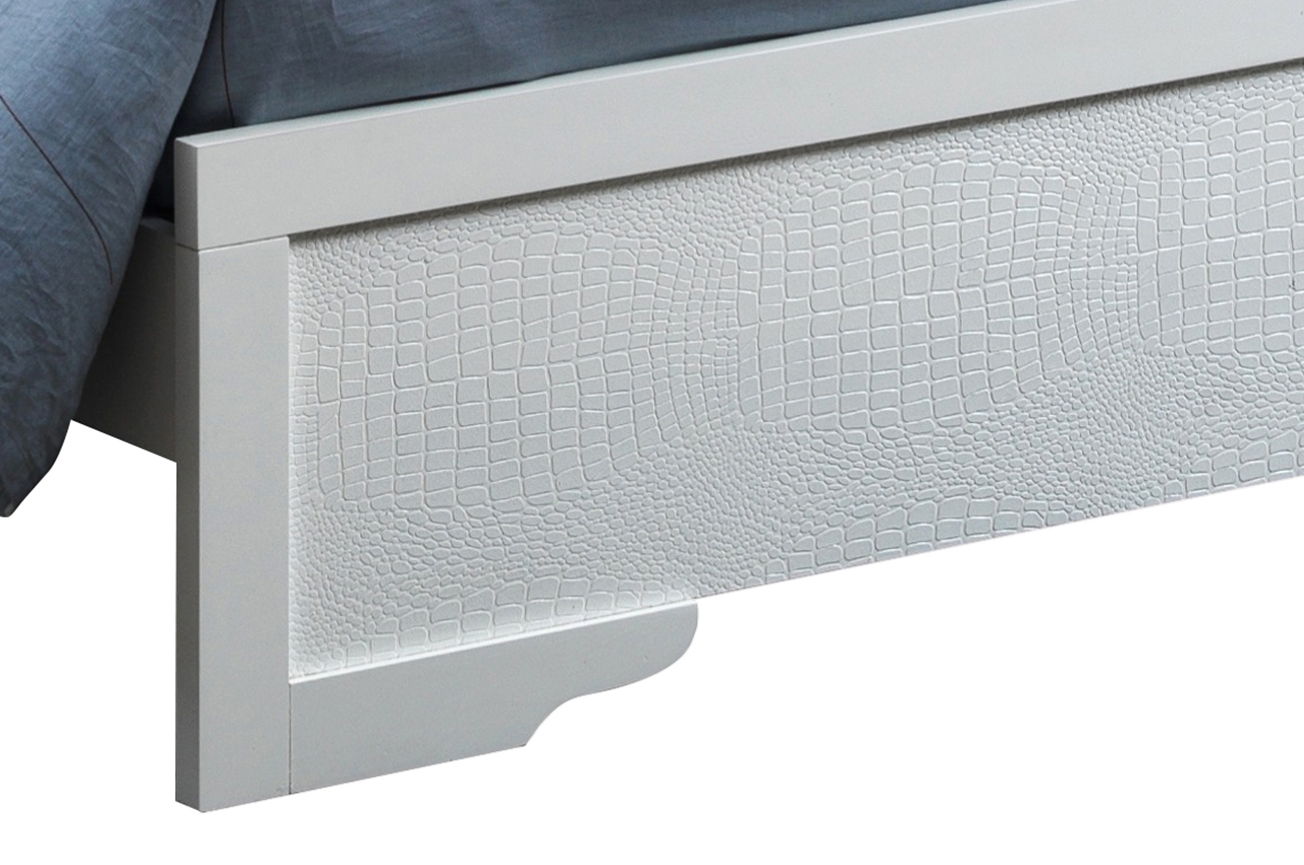 A close-up of the Lorana - G6590C-FB3 Full Bed's silver champagne footboard, featuring a textured crocodile-skin-like pattern. Bedding is partially visible in the upper left corner.