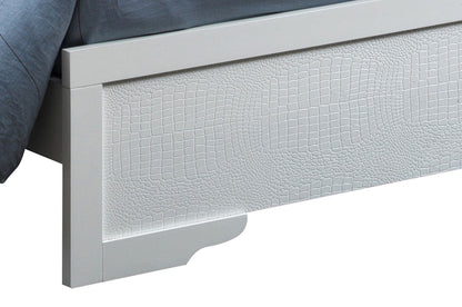 A close-up of the Lorana - G6590C-FB3 Full Bed's silver champagne footboard, featuring a textured crocodile-skin-like pattern. Bedding is partially visible in the upper left corner.