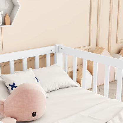 A Double Floor Bed With Fence and Guardrails, without door, is set in a nursery featuring pale bedding, a plush pink whale toy, a blue X-patterned pillow, beige paneled walls, and pastel house-shaped decorations.