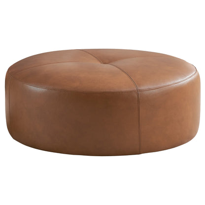 The Rochelin - Ottoman - Tan features a round, tan leather design with visible stitching and a smooth, cushioned surface, shown against a plain white background.