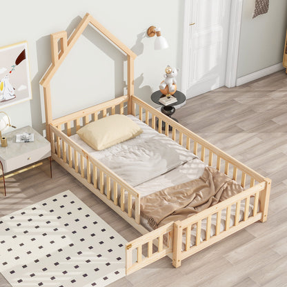 The House-Shaped Headboard Floor Bed With Fence features a natural wood frame, light bedding, a small pillow, and a safety rail. The room has a light palette, dark-dotted rug, and bedside table with toys.