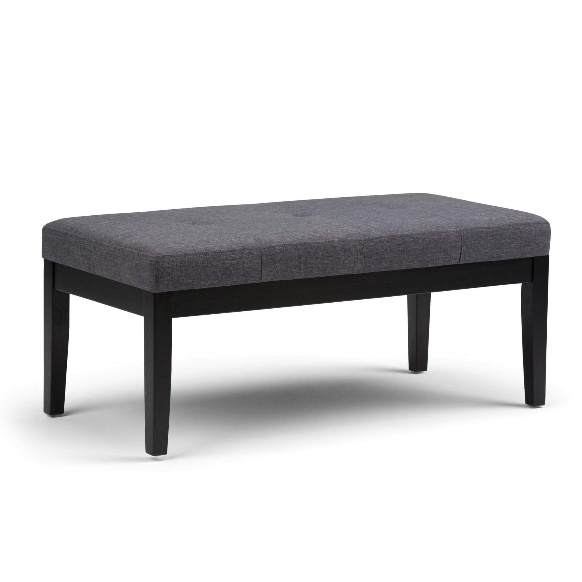 The Lacey Upholstered Tufted Ottoman Bench features dark wooden legs and a cushioned gray seat in a simple modern design, shown on a white background.