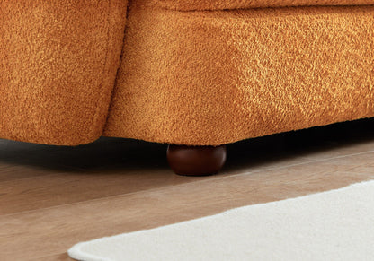 Close-up of the bottom corner of the Paton - Comfortable Sofa in orange texture, featuring a rounded dark wooden leg on a light wood floor beside a white rug.