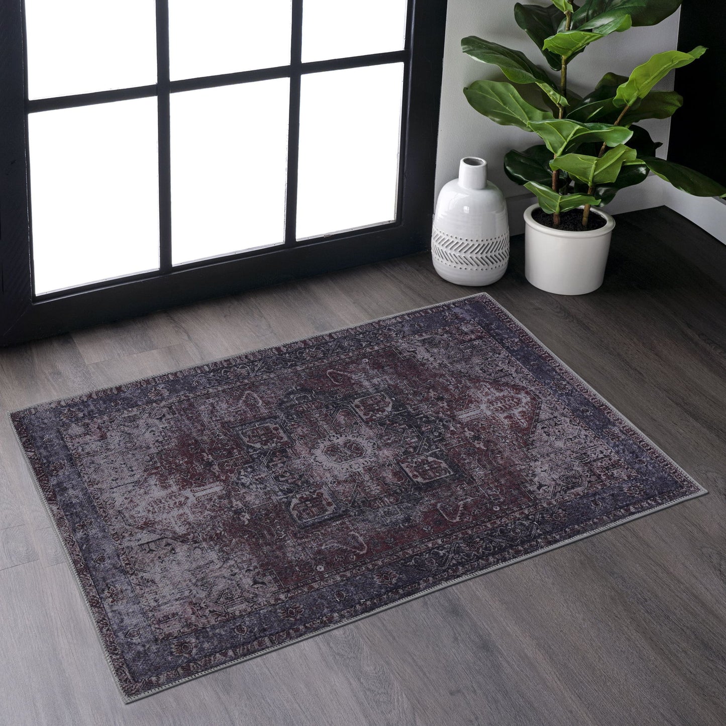 The Maval - Unique Washable Area Rug adds charm to gray wood floors near a large window. A potted plant and white decorative vase in the corner are brightened by natural sunlight.