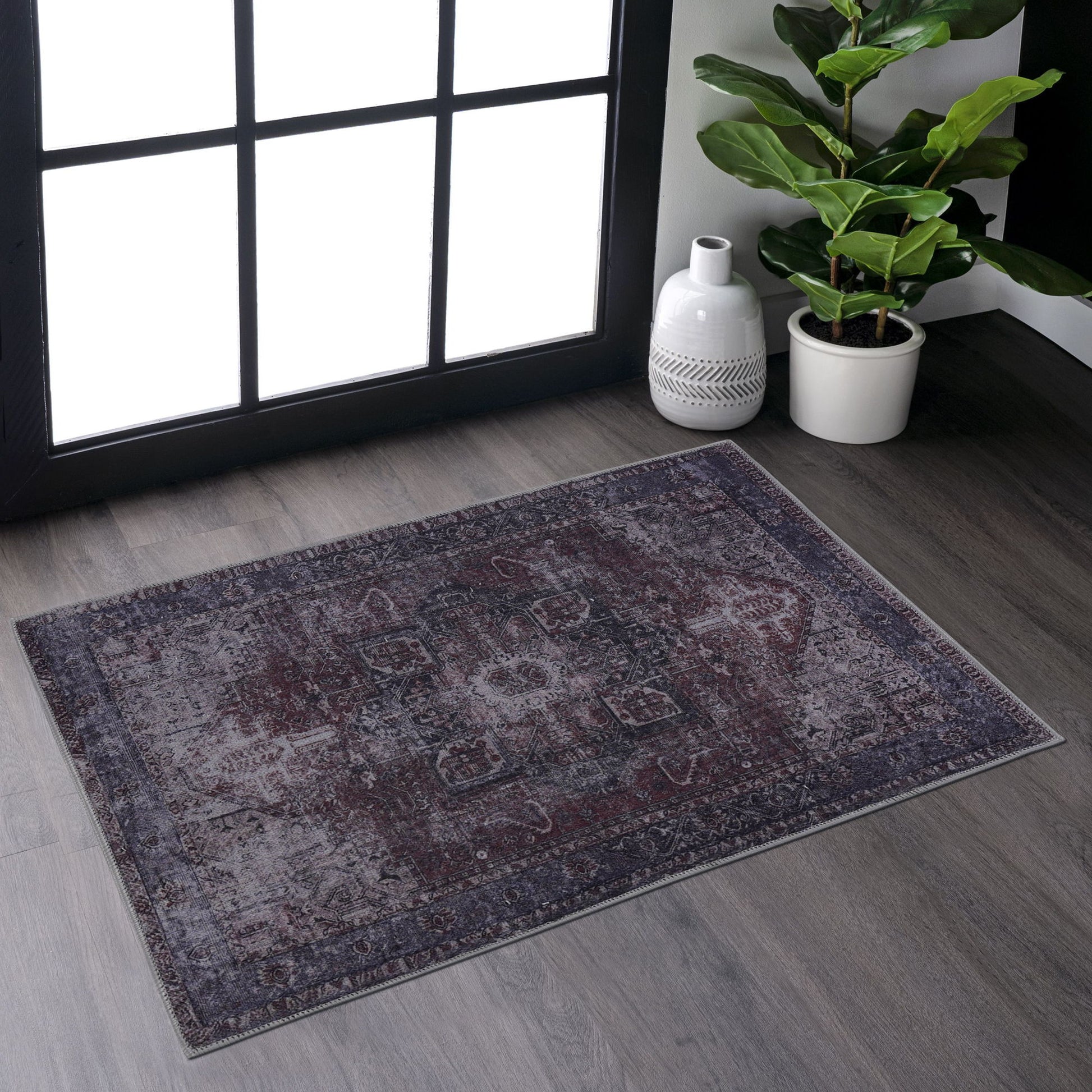 The Maval - Unique Washable Area Rug adds charm to gray wood floors near a large window. A potted plant and white decorative vase in the corner are brightened by natural sunlight.