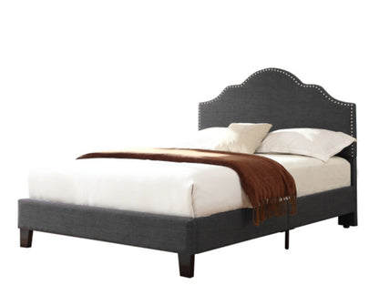 The Kopa - Fabric Upholstered Bed features a dark gray frame with a scalloped, studded headboard, styled with white bedding, two cream pillows, and a brown throw blanket against a plain white background.
