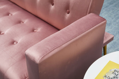 Close-up of the Comfort Compact Design Sofa Bed in pink velvet with button tufting, focusing on the armrest and seat. A white round table with a yellow object and gray item appears in the corner.