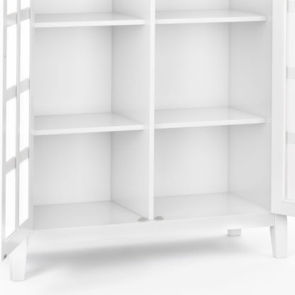 A close-up of the Acadian - Medium Storage Cabinet, Handcrafted, featuring four shelves and glass-paneled doors, empty and standing on short legs against a plain background.