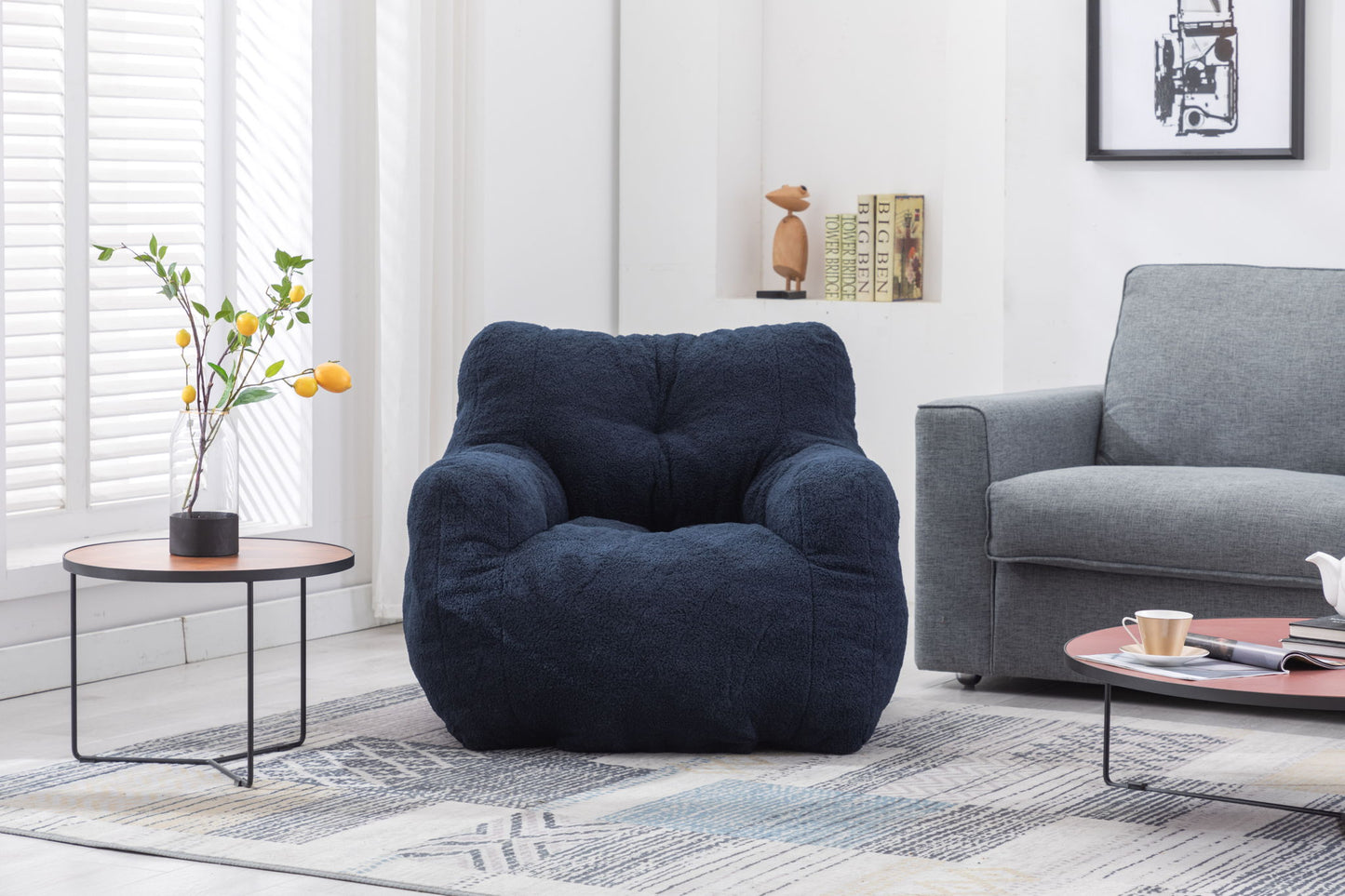 A Soft Teddy Fabric Tufted Foam Bean Bag Chair sits on a patterned rug between a small round table with yellow flowers and a light gray sofa in a bright, modern living room.