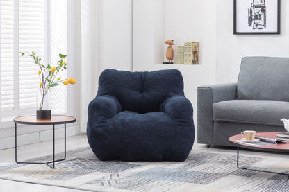A Soft Teddy Fabric Tufted Foam Bean Bag Chair sits on a patterned rug between a small round table with yellow flowers and a light gray sofa in a bright, modern living room.
