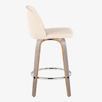 A side view of the Toriano Contemporary Fixed Height Counter Stool, featuring a light beige cushioned seat and backrest, wooden legs, and a round chrome footrest, shown against a plain white background. Set includes 2 stools with swivel functionality.