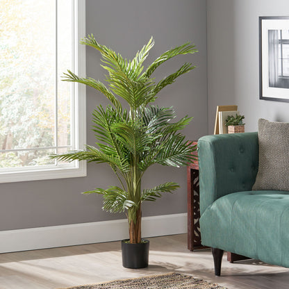 An Artificial Palm Tree in a black pot sits beside a green sofa in a modern living room with gray walls and a large window.