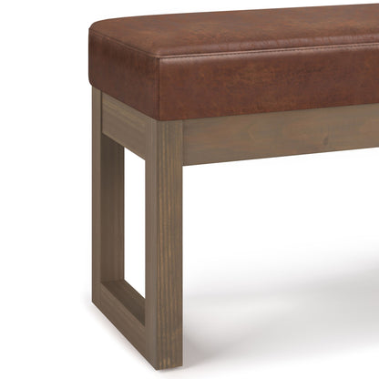 The Milltown Upholstered Ottoman Bench features a brown faux leather cushioned seat and a rectangular wooden base with an open square leg design.