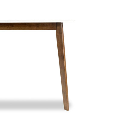 A close-up of the Carlos Dining Table showcases one wooden leg and part of the underside, with a white tabletop against a plain white background.