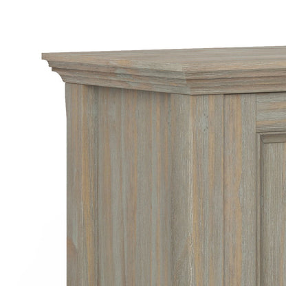 A close-up of the Amherst - Handcrafted Low Storage Cabinet’s top corner shows its light grayish-brown finish, vertical wood grain texture, and a decorative beveled edge at the top.