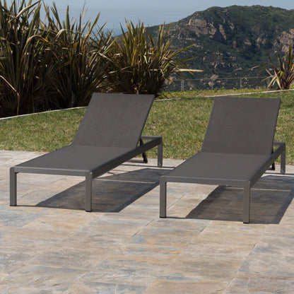 Two Outdoor Patio Chaise Lounges with 5 reclining positions are placed on a stone patio, surrounded by grass and tall plants, with mountains visible in the background under a clear sky.