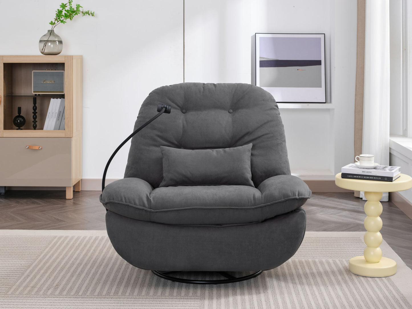 A cozy Power Recliner Swivel Glider with USB charger and Bluetooth music player sits on a beige rug. Next to it is a round yellow side table with books, and behind, a cabinet with decor and a framed picture against a white wall.