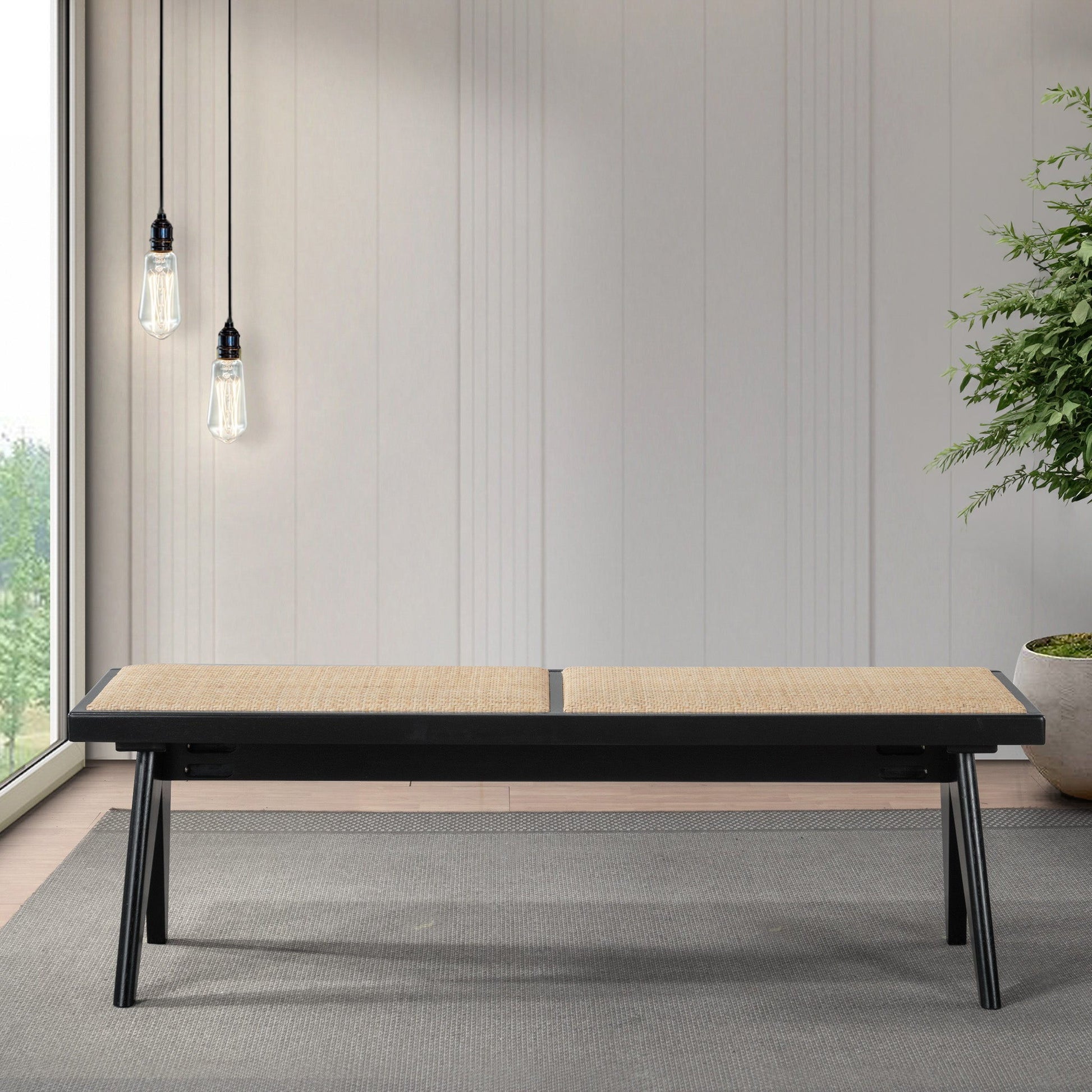 The Keira - Modern Aesthetics Bench, featuring a light woven seat and black frame, stands on a gray rug in a bright room with light wood panel walls, pendant lights, and a potted plant.