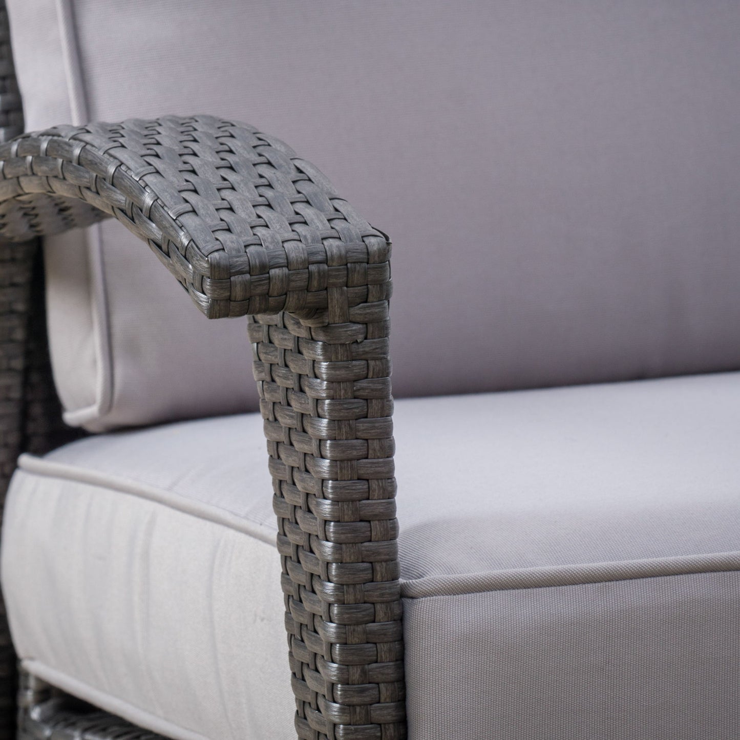 Close-up of the Honolulu - Wicker Set Outdoor Seating, highlighting the wicker armrest and light gray cushioned seat and backrest, which display the woven texture and soft fabric.