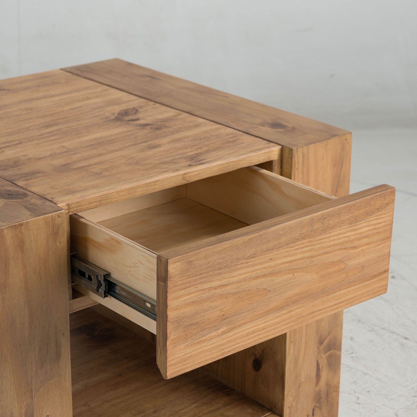 A close-up of the Harlan End Table in oak shows its sturdy, rectangular build with light wood grain. The open drawer reveals the interior and metal sliding mechanism, highlighting quality craftsmanship.