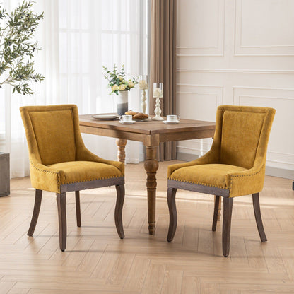 Two Ultra Side Dining Chairs with thickened mustard-yellow fabric and neutral solid wood legs, accented by bronze nail heads, sit at a wooden dining table set for breakfast in a light-filled room with wood floors and large windows.