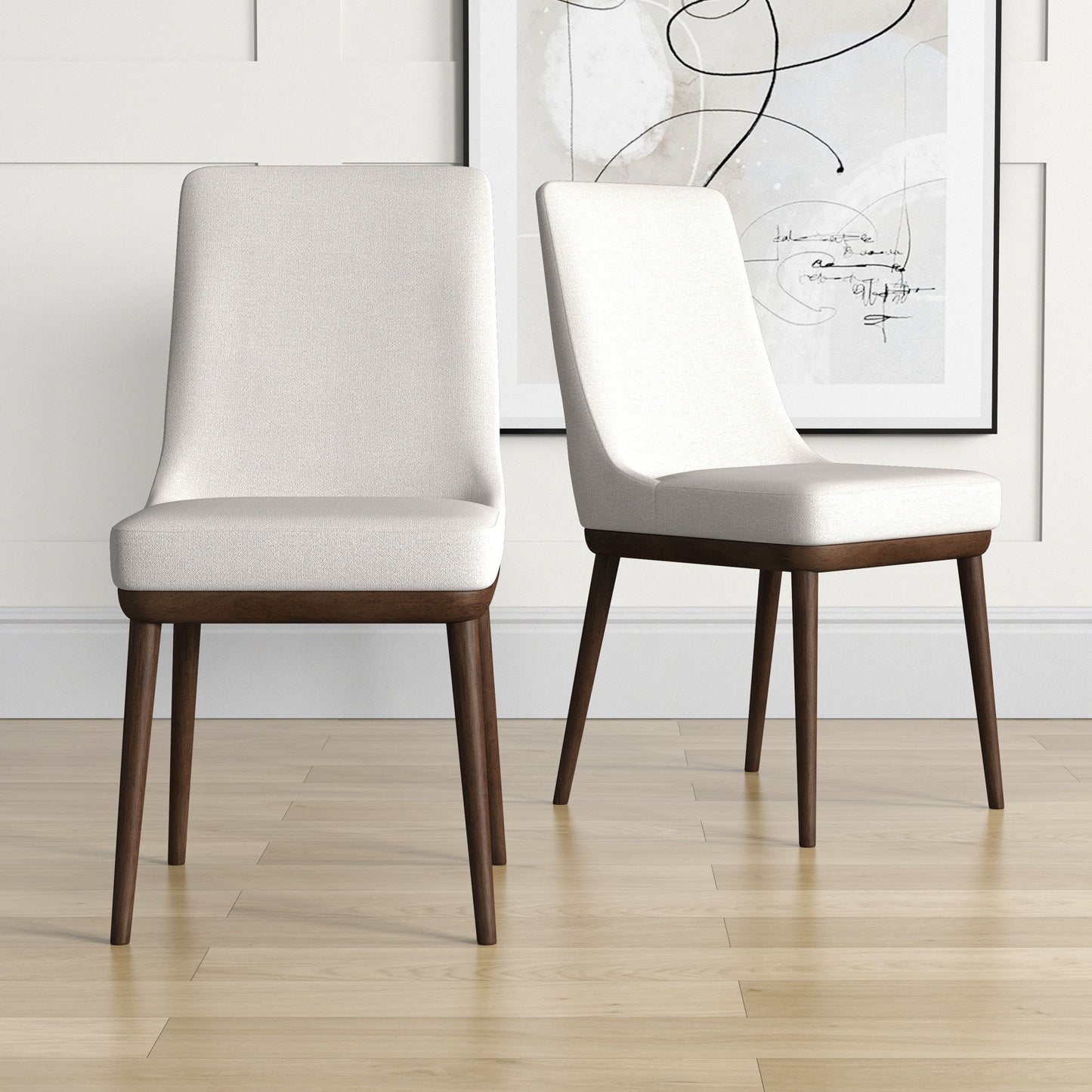 Two Kate Mid-Century Modern Dining Chairs with light upholstered seats and dark wooden legs sit on a light wood floor, with a framed abstract artwork hanging on the white paneled wall behind.