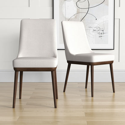 Two Kate Mid-Century Modern Dining Chairs with light upholstered seats and dark wooden legs sit on a light wood floor, with a framed abstract artwork hanging on the white paneled wall behind.