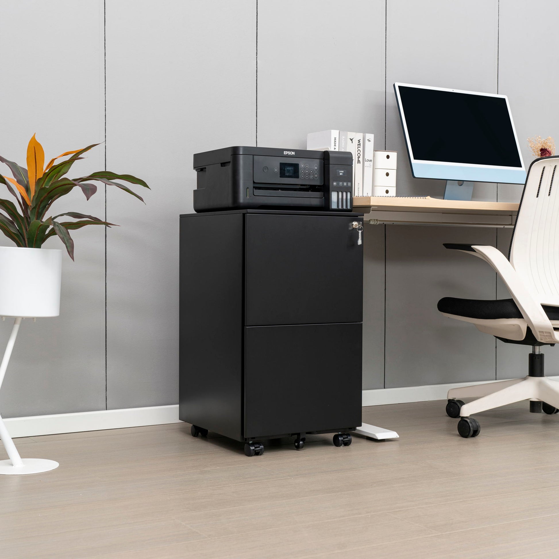 A modern office features a black printer on the 2 Drawer File Cabinet With Lock, a desk with a computer, a white chair, and a potted plant on a stand against a gray wall and light wood floor.