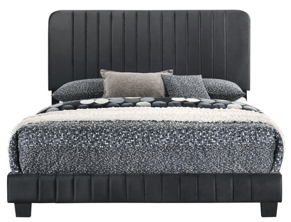 The Lodi - Bed features a tall, dark upholstered headboard and frame, styled with patterned black, white, and gray bedding, and accented by decorative pillows in matching hues.