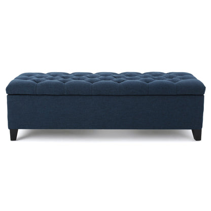 The Glouster Contemporary Storage Ottoman features a rectangular, dark blue upholstered body, button tufted top, and short black legs, displayed against a white background.