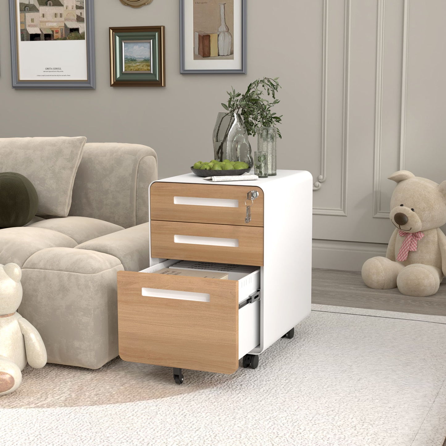 A modern living room features a beige sofa, framed art, decorative plants and bottles, two plush teddy bears, and a white and wood 3 Drawer Mobile File Cabinet Under Desk Office with open drawers and 5-wheel anti-tilting design.