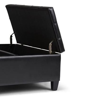 The Harrison Large Coffee Table Storage Ottoman, shown with its cushioned black lid open to reveal spacious internal storage, features short square legs and is set against a white background.