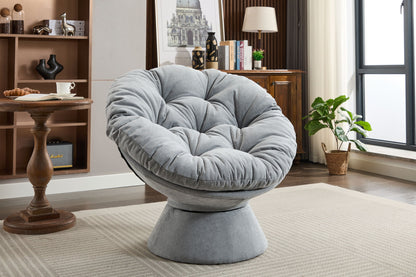 An Oversized Swivel Accent Chair, 360 Swivel Barrel Chair, Papasan Chair for living room, sits on a beige rug in a modern space with a wooden table, potted plant, bookshelf, and large window letting in natural light.