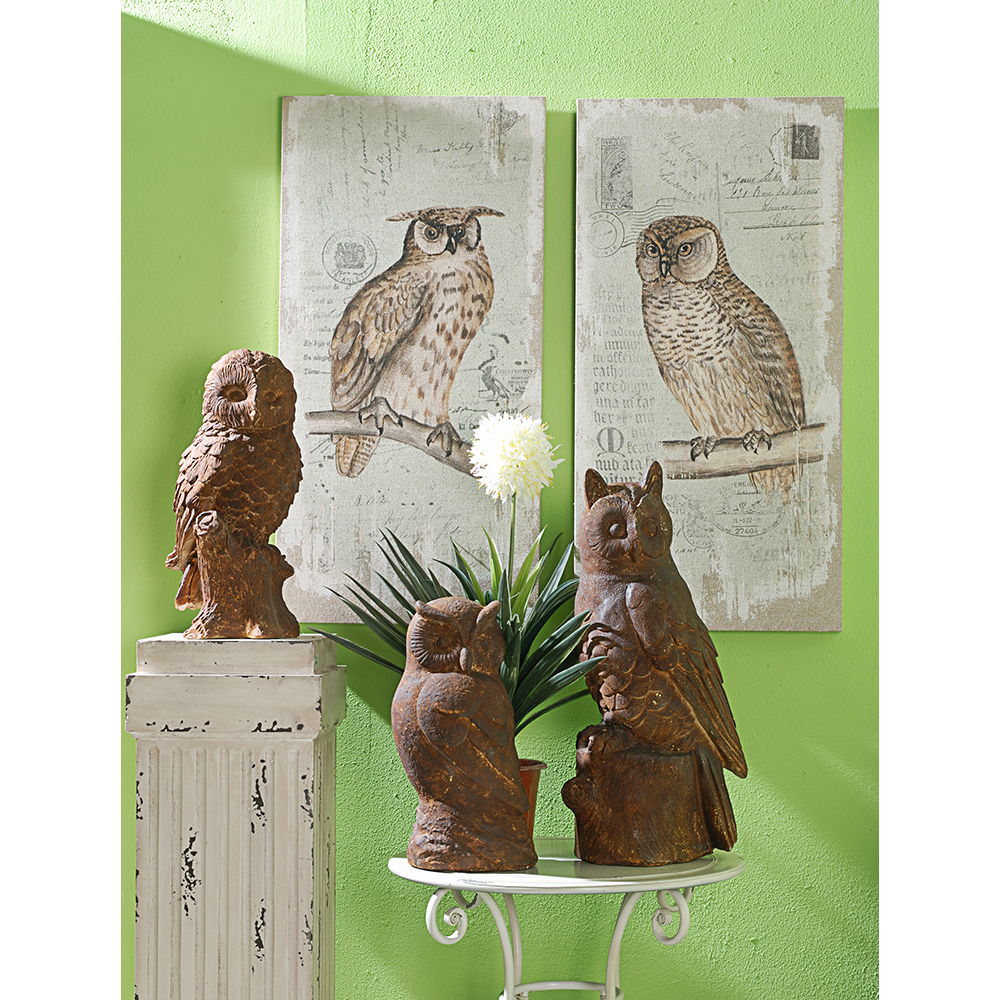 A display features two Lilith Owl Prints With Distressed Look, Rectangle Animal Hanging Wall Art (Set of 2) - Multicolor on a green wall, with four brown owl sculptures on a white pedestal and table near a potted plant with white flowers.