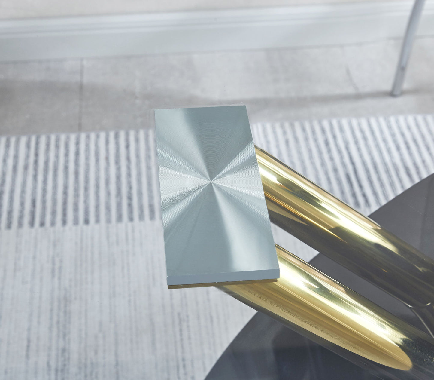 A close-up of the Stylish Dining Room Table, featuring a luxury black glass top and modern angled gold legs, set on a gray and white striped carpet.
