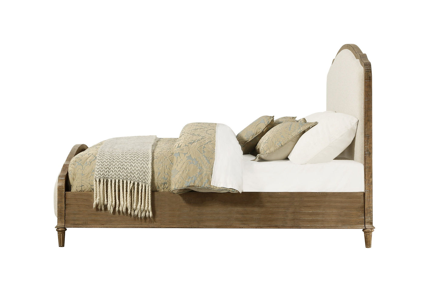 Side view of the Ludin - Upholstered Bed with a cushioned headboard, white bedding, patterned pillows, and a beige throw blanket folded at the foot.