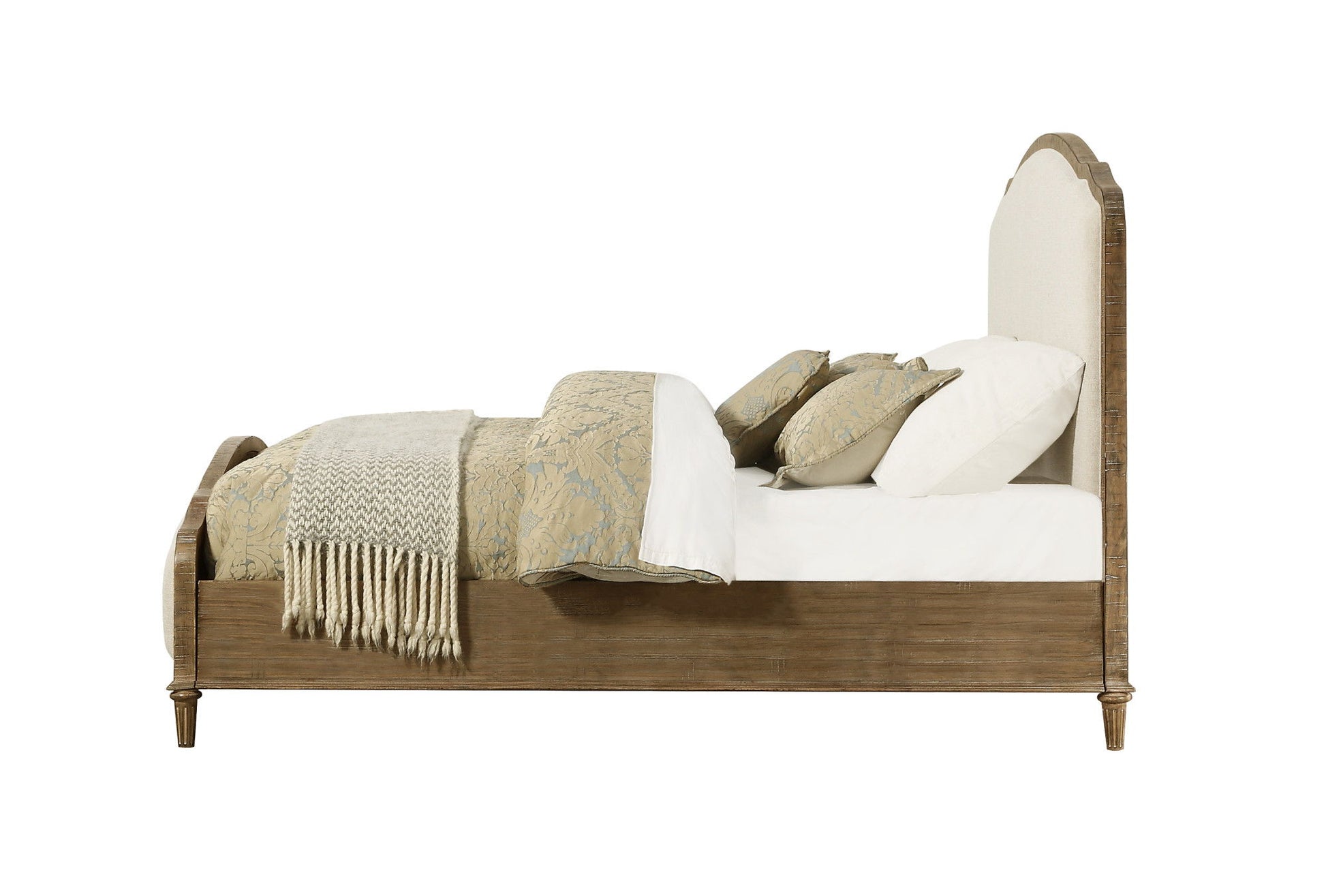 Side view of the Ludin - Upholstered Bed with a cushioned headboard, white bedding, patterned pillows, and a beige throw blanket folded at the foot.