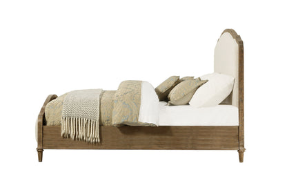 Side view of the Ludin - Upholstered Bed with a cushioned headboard, white bedding, patterned pillows, and a beige throw blanket folded at the foot.