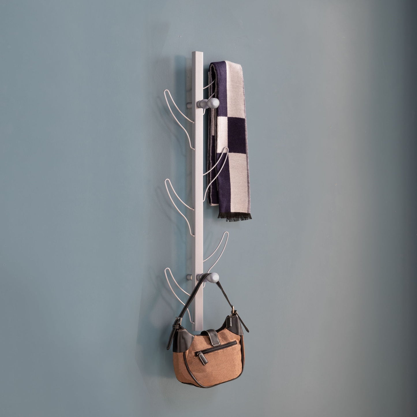 A Vertical Eight Hook Coat Rack Wall Mount displays a black-and-white striped scarf and a tan handbag against a plain blue wall.