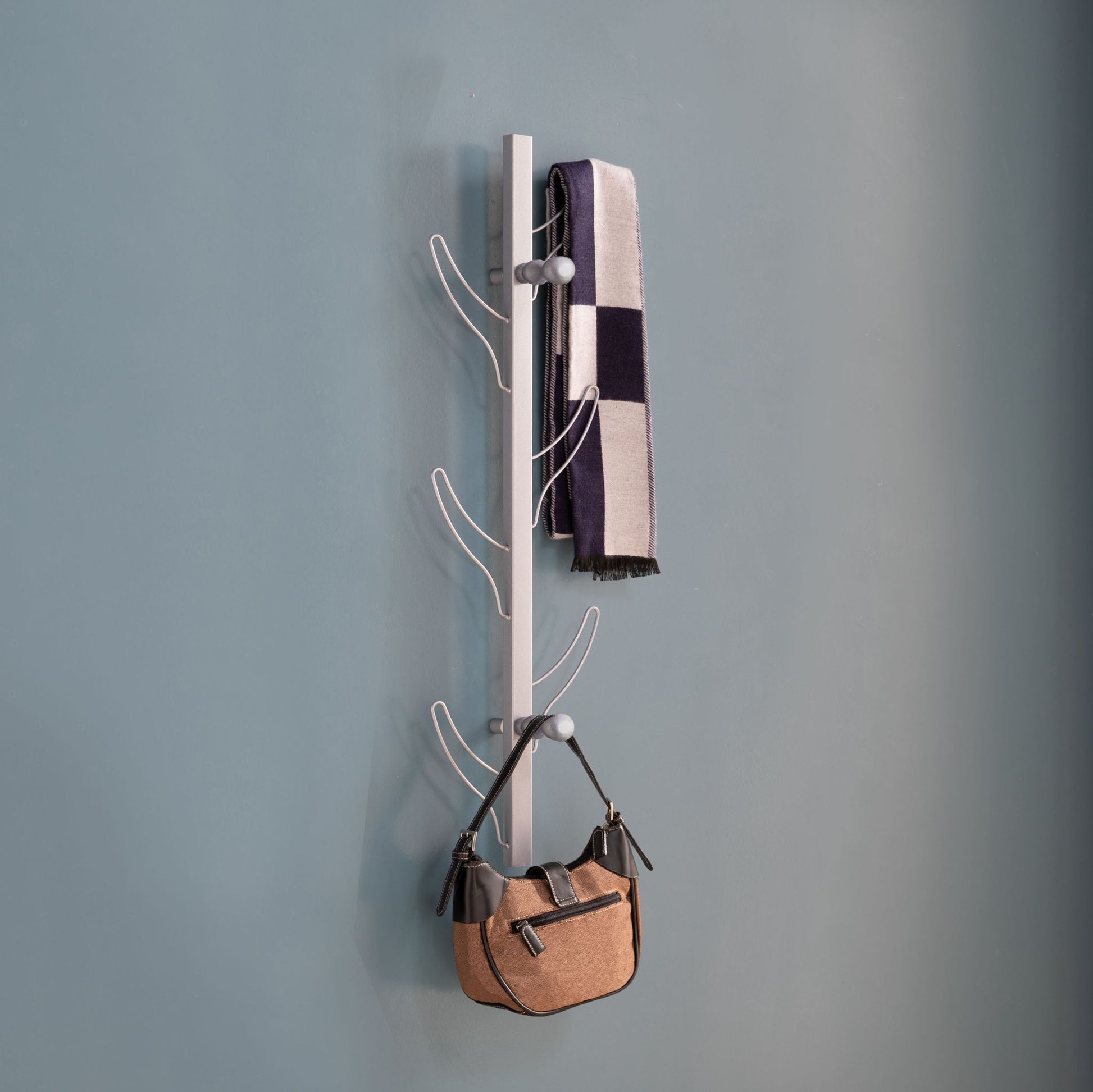 A Vertical Eight Hook Coat Rack Wall Mount displays a black-and-white striped scarf and a tan handbag against a plain blue wall.
