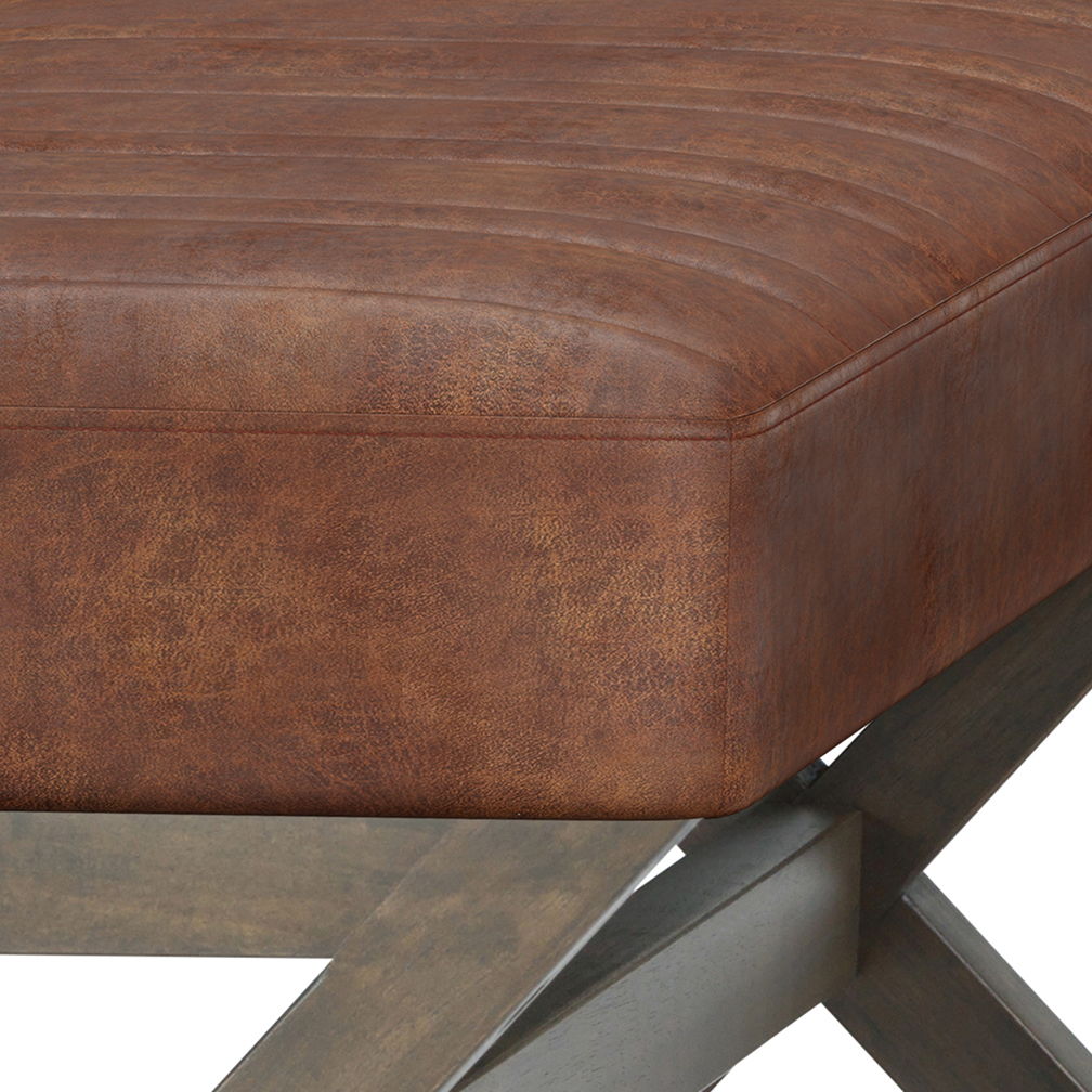 Close-up of the Salinger - Large Upholstered Ottoman Bench featuring brown distressed leather cushions, visible stitching, and a smooth-finished wooden X-shaped leg frame.