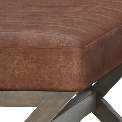 Close-up of the Salinger - Large Upholstered Ottoman Bench featuring brown distressed leather cushions, visible stitching, and a smooth-finished wooden X-shaped leg frame.