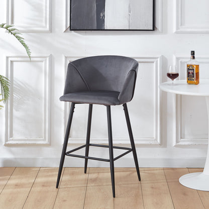 A set of modern gray Counter Height Bar Stools with black metal legs sits by a round white table holding red wine and liquor, against white paneled walls with a potted plant on the left.