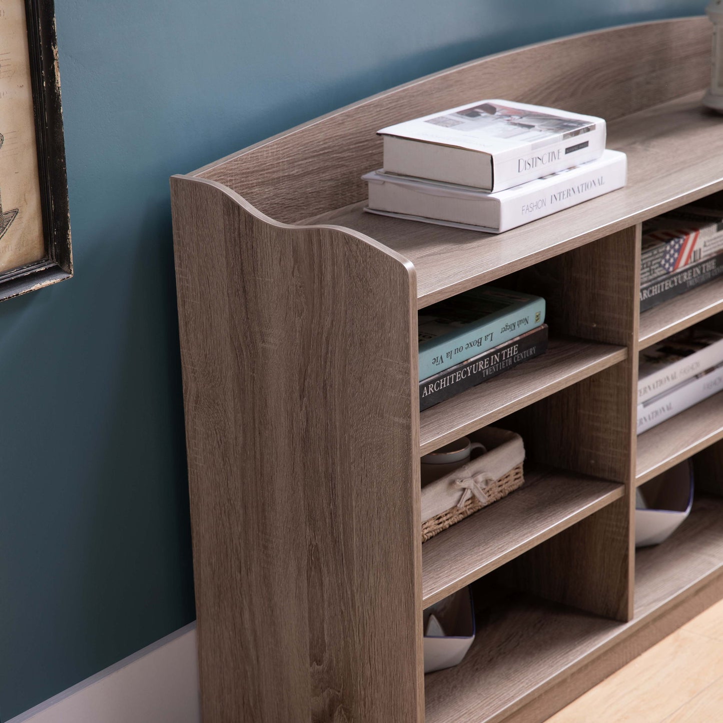 An Entryway Shoe Storage Bench with nine storage shelves serves as an entryway organizer against a blue wall, with shoes and decorative items neatly arranged on its shelves and top surface.