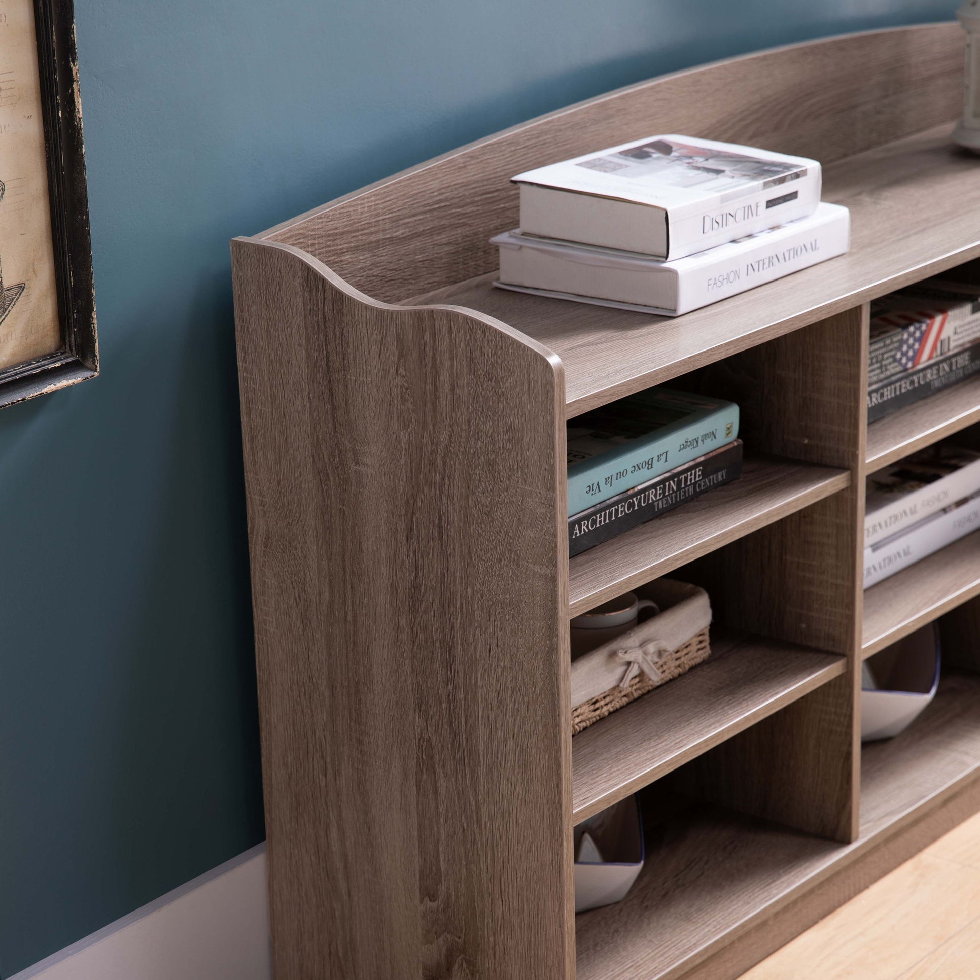An Entryway Shoe Storage Bench with nine storage shelves serves as an entryway organizer against a blue wall, with shoes and decorative items neatly arranged on its shelves and top surface.