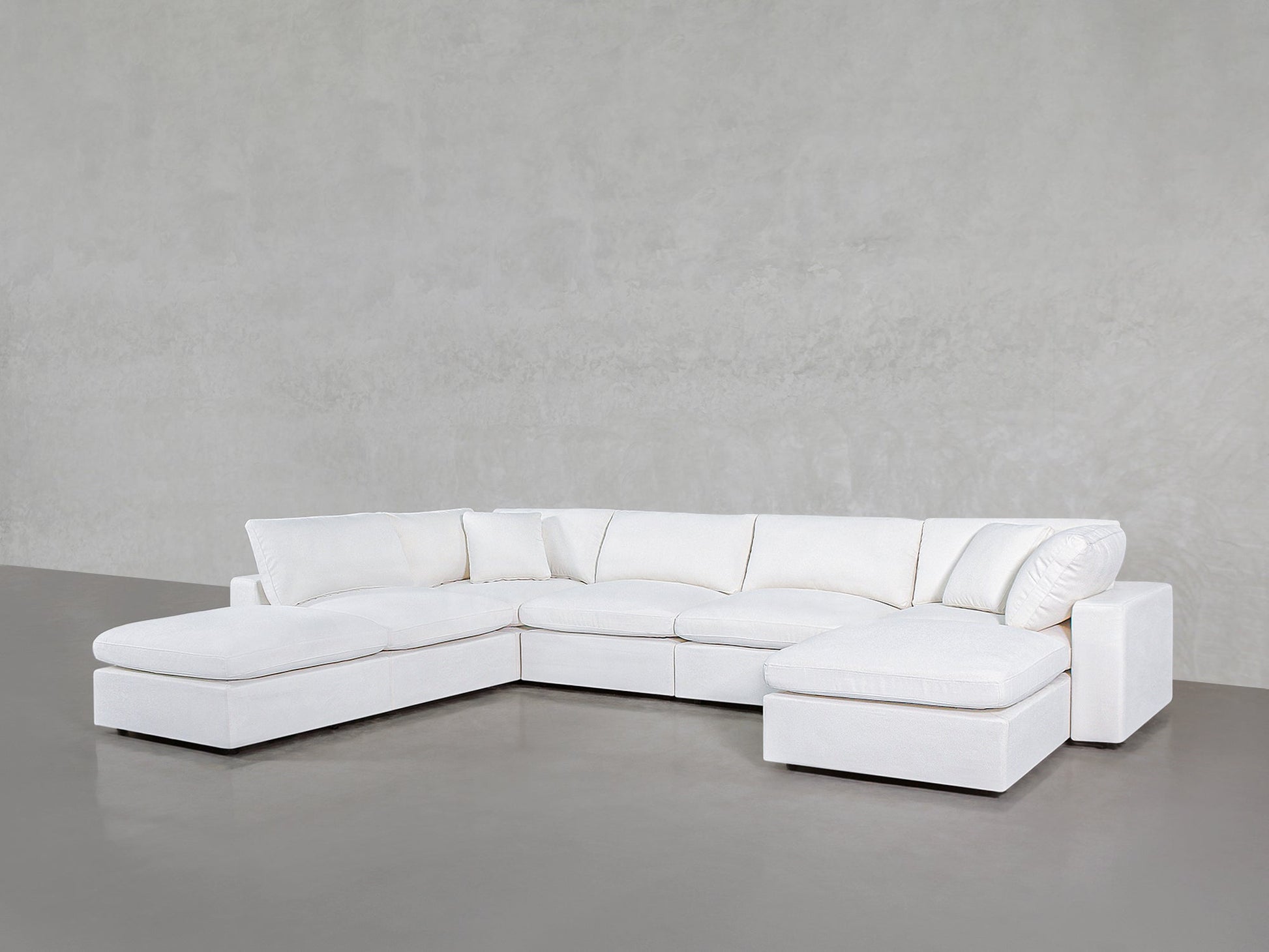 The 7-Seat Modular Chaise Corner Lounger Sectional, featuring plush white cushions, is arranged in an L-shape along a plain light gray wall and floor.
