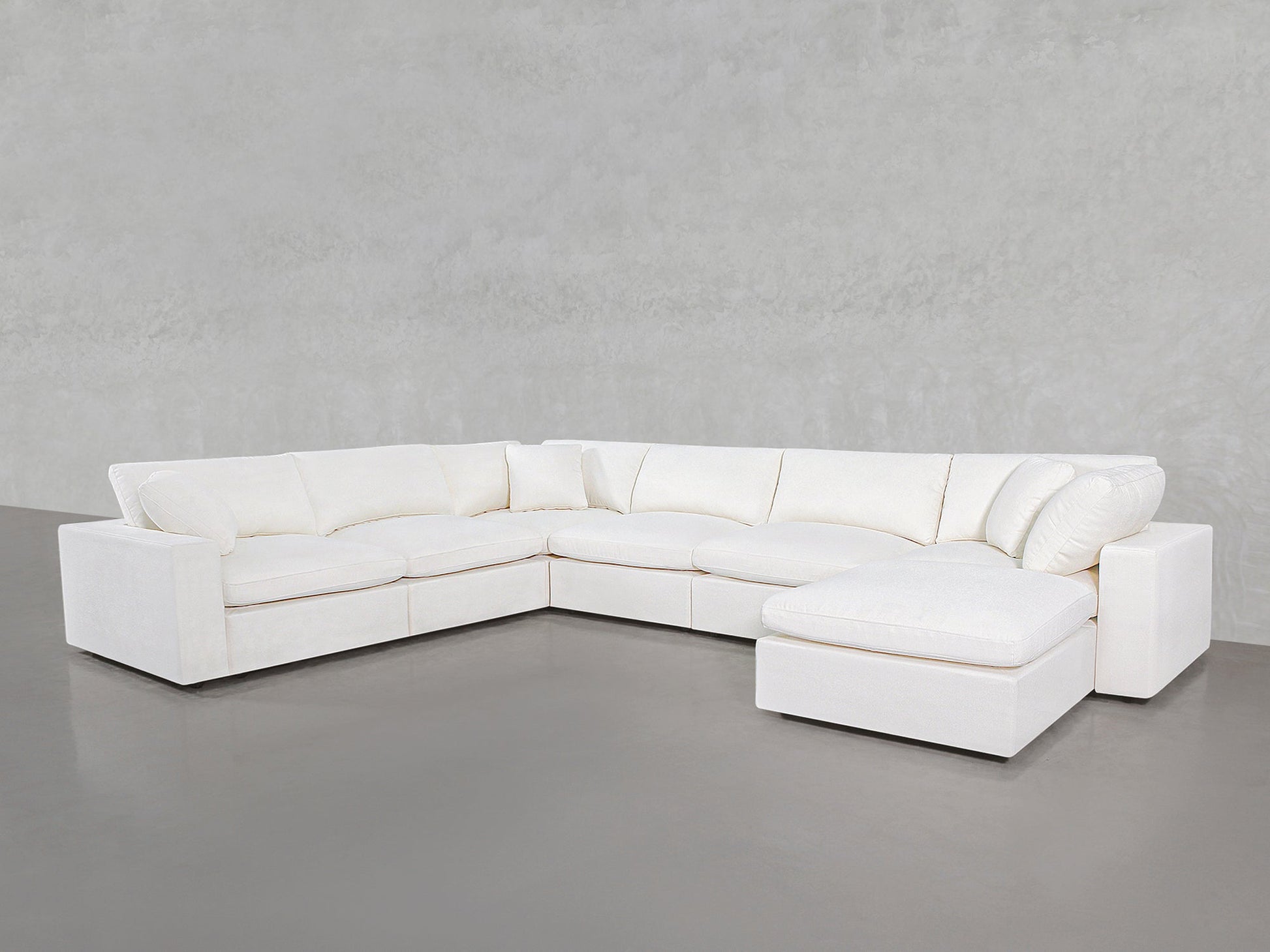 A spacious 7-Seat Modular Chaise Corner Sectional with plush cushions is set against a plain, light gray wall and floor.