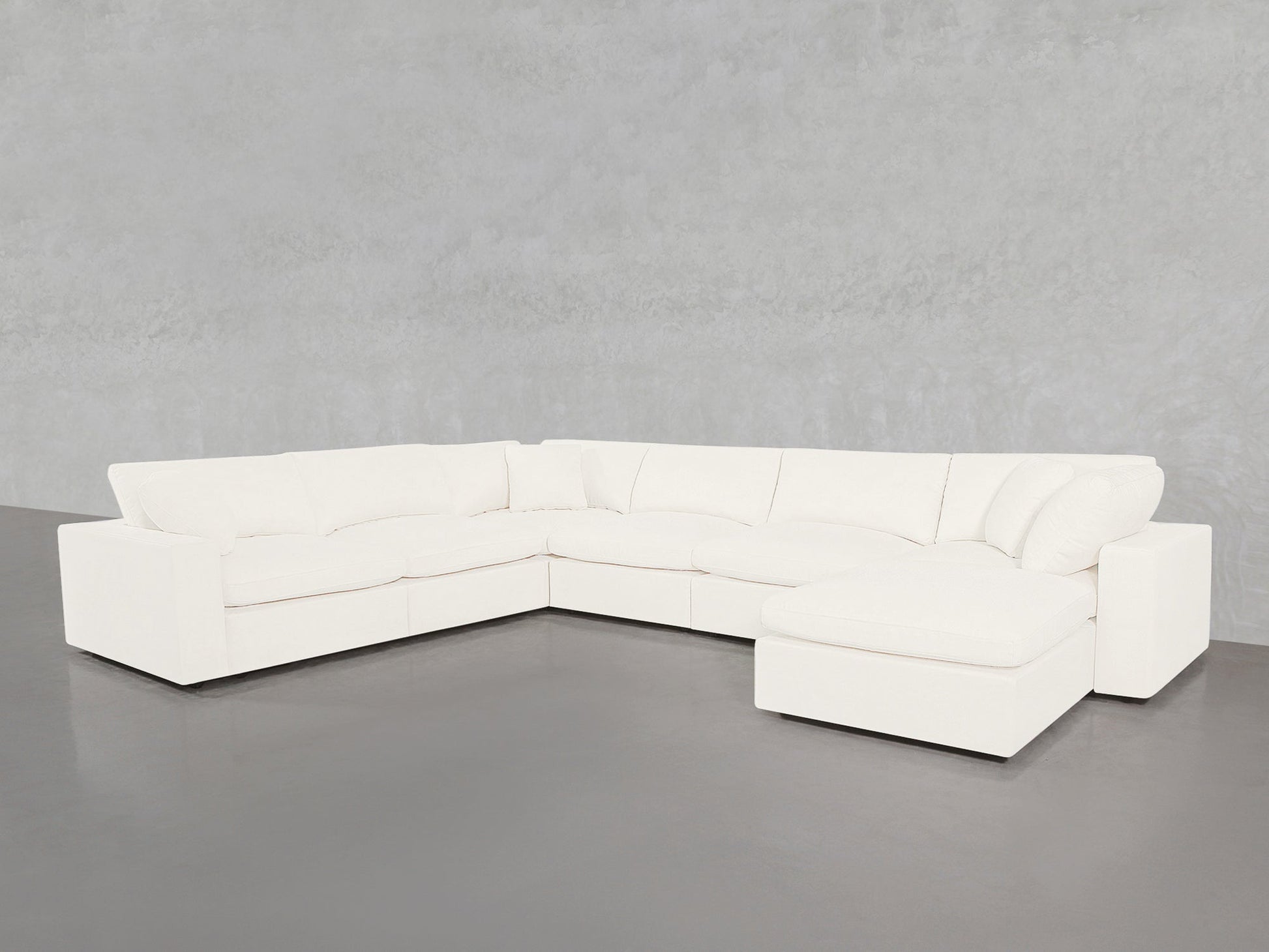 The 7-Seat Modular Chaise Corner Sectional, featuring thick cushions and a right-side chaise, is set on a gray floor against a light gray textured wall.