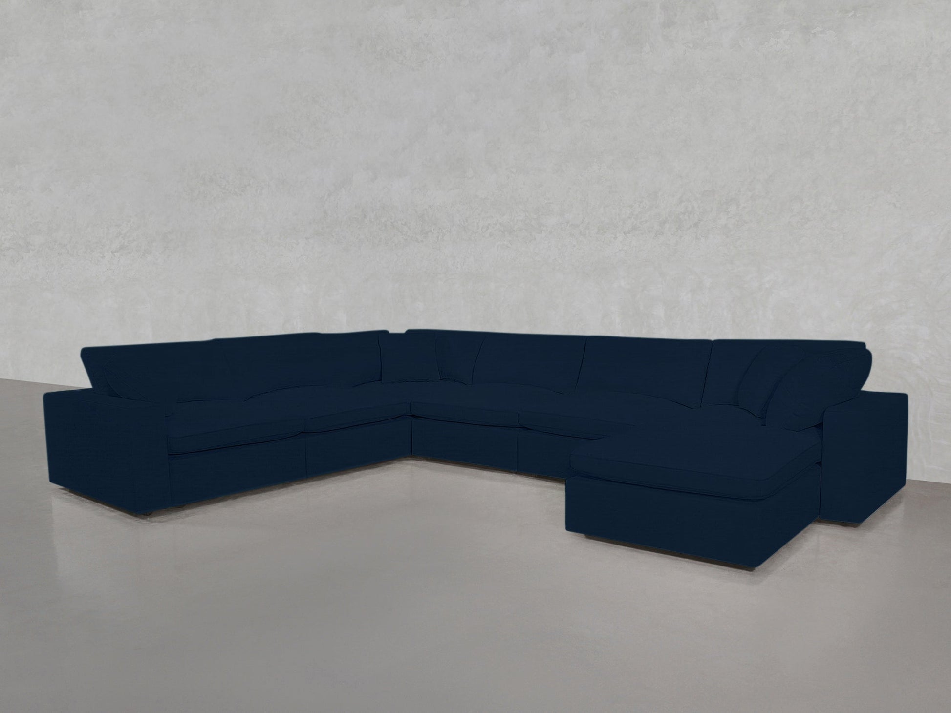 A 7-Seat Modular Chaise Corner Sectional in dark blue is arranged in a minimalist room featuring light gray walls and a smooth, light-colored floor.