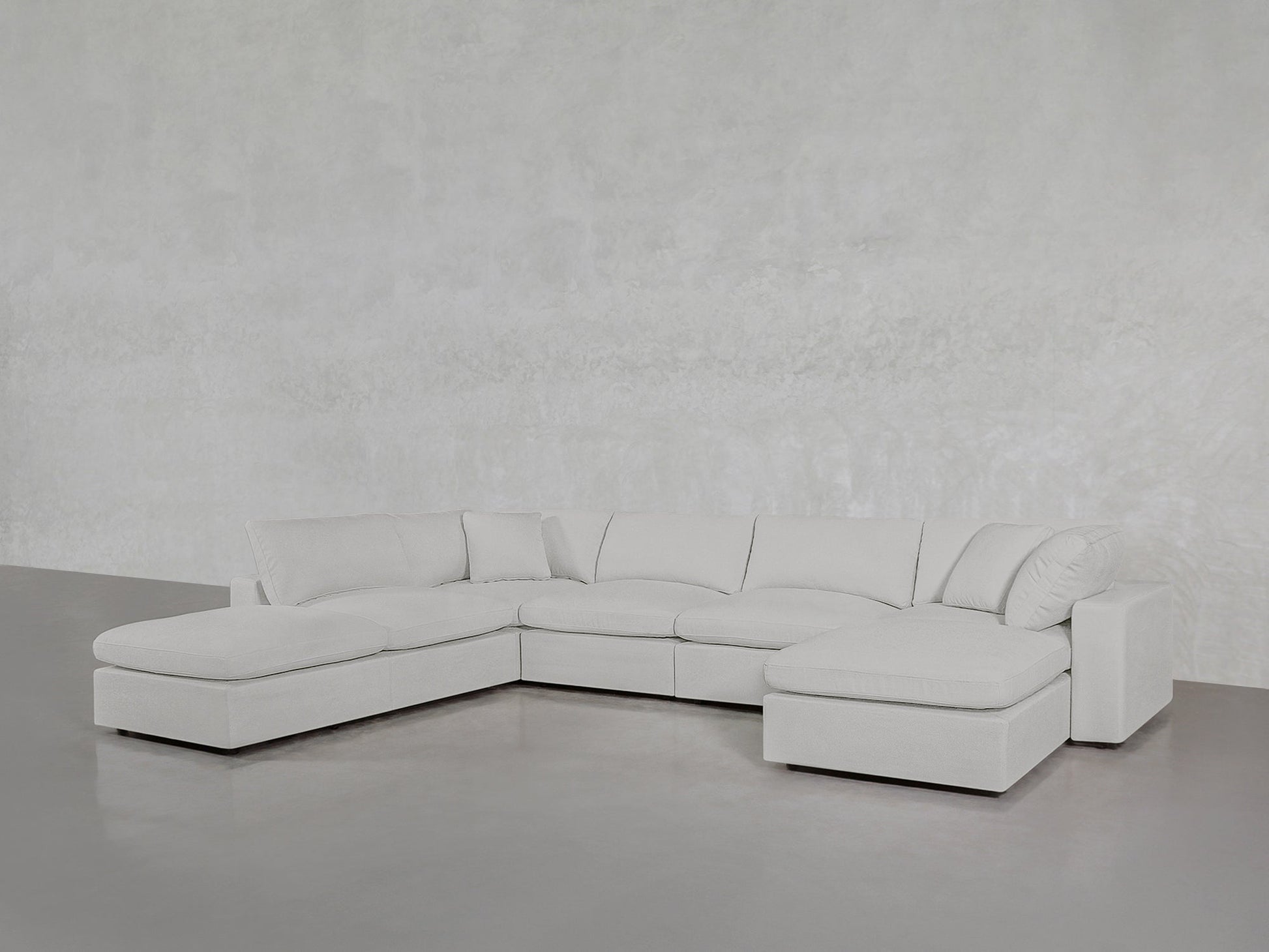 The 7-Seat Modular Chaise Corner Lounger Sectional in light gray features chaise lounges on both ends and sits on a polished concrete floor against a textured light gray wall.